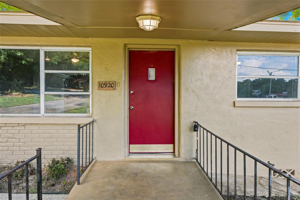 A red front door is centered on a beige exterior wall with metal railings — 10920 SE 55TH AVENUE, BELLEVIEW, FL