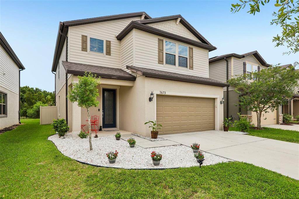 A two-story suburban house with beige siding, a tan garage, and a white gravel garden — 7673 YALE HARBOR DRIVE, WESLEY CHAPEL, FL