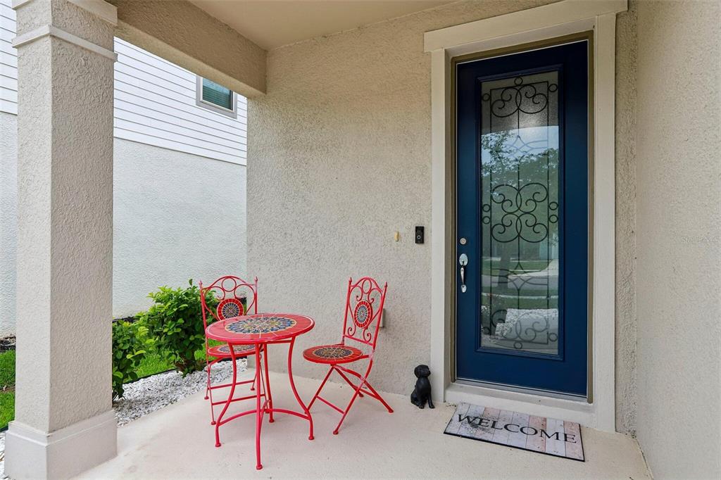A covered porch features a blue front door, a bistro set, and a welcome mat — 7673 YALE HARBOR DRIVE, WESLEY CHAPEL, FL