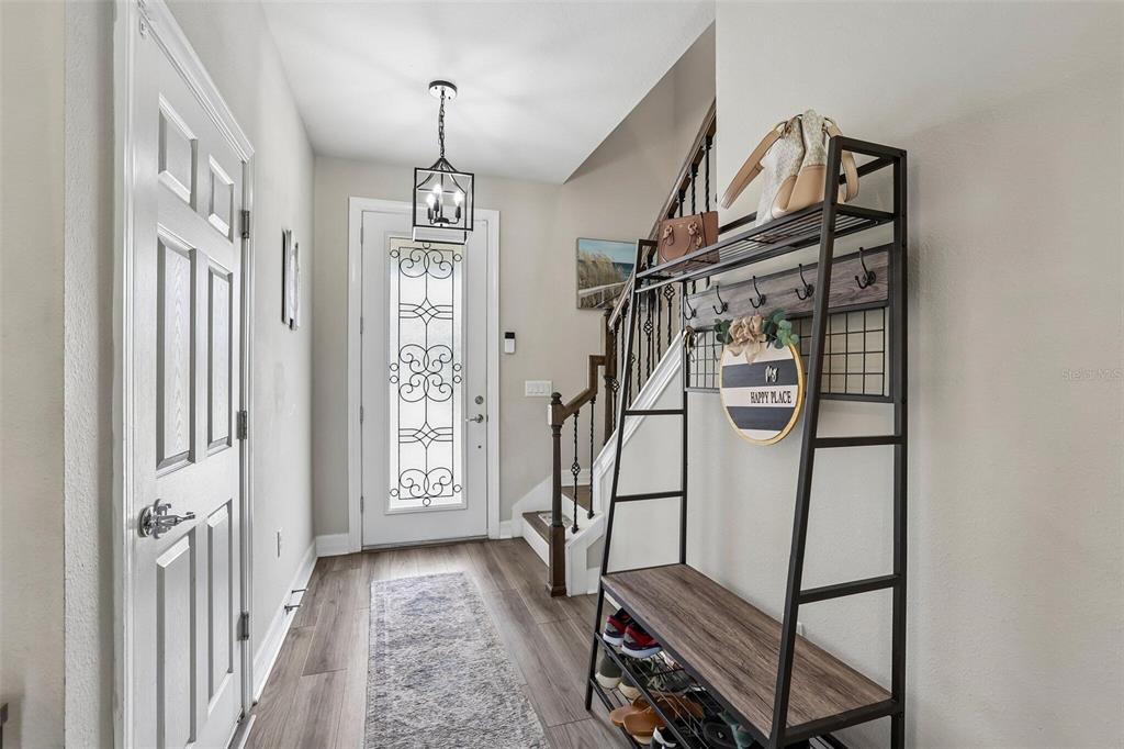 An entryway features wood-look flooring, a staircase with iron railings, and a metal hall tree — 7673 YALE HARBOR DRIVE, WESLEY CHAPEL, FL