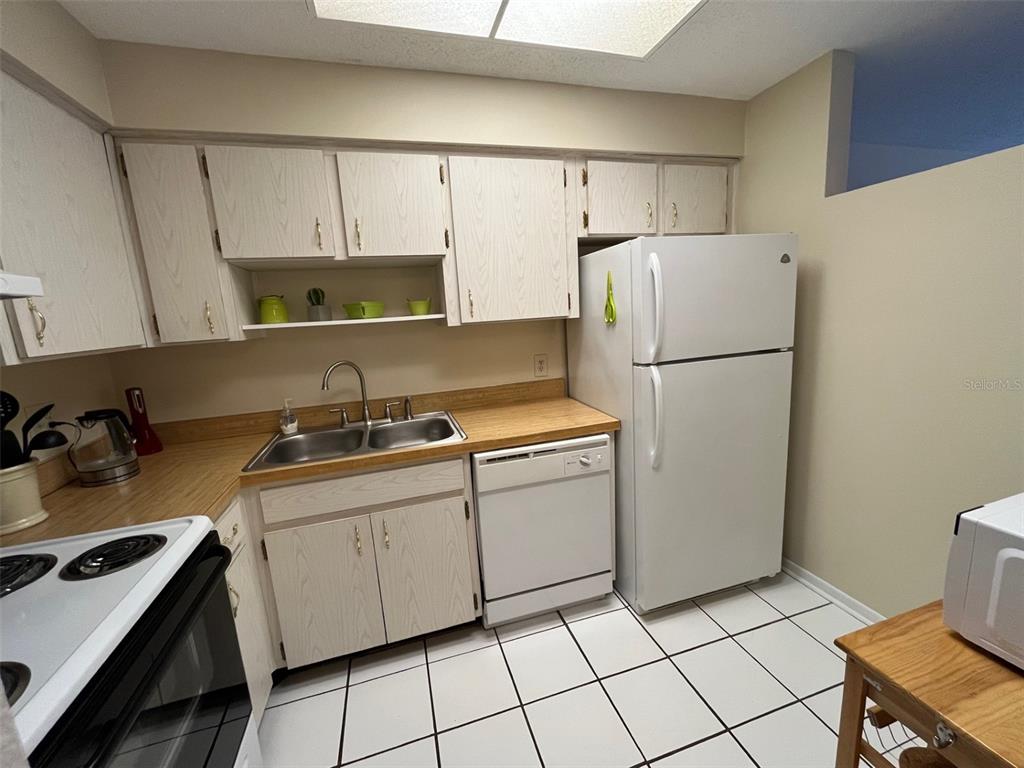 A kitchen features light wood cabinets, white appliances, a double sink, and white tile flooring — 670 GREEN VALLEY ROAD UNIT F5, PALM HARBOR, FL