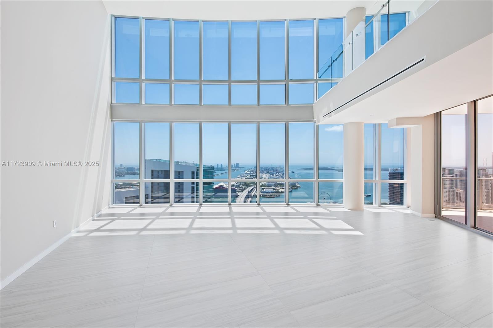 A bright, empty living room features double-height floor-to-ceiling windows with expansive city and water views — 851 NE 1st Ave # 5411, Miami FL 33132, MIAMI, FL
