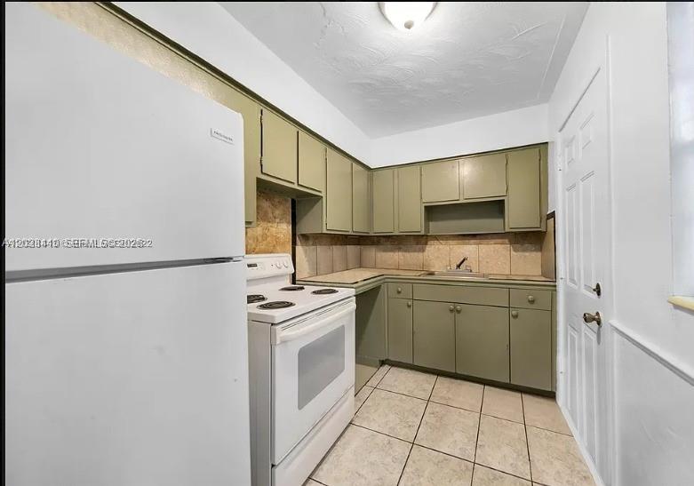 A small kitchen features olive green cabinets, white appliances, tiled flooring, and a tiled backsplash — 1500 NW 69th Ter, Miami FL 33147, MIAMI, FL