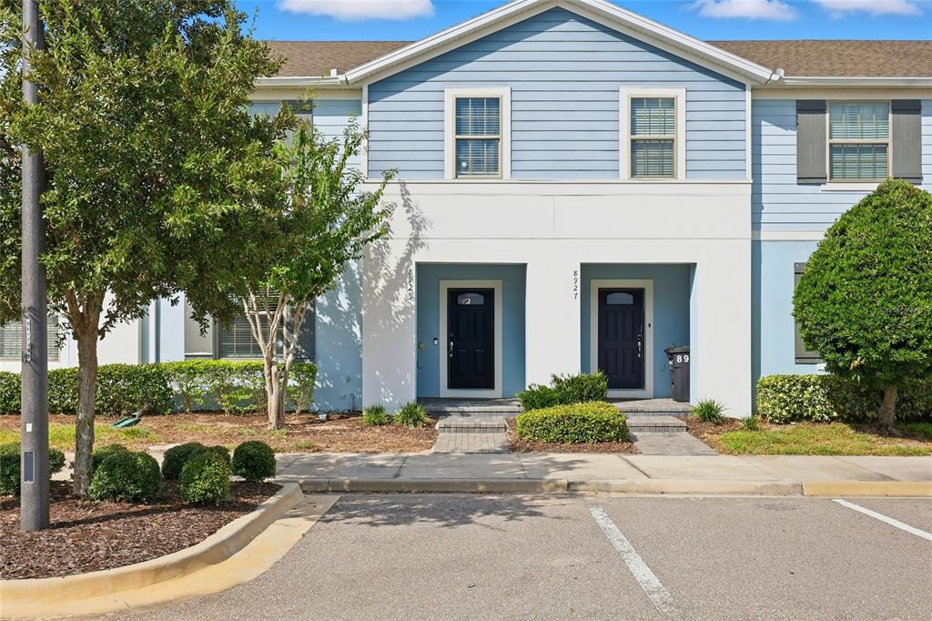 A two-story townhouse exterior features light blue siding, white trim, and two black front doors — 8929 SYDNEY AVENUE, KISSIMMEE, FL