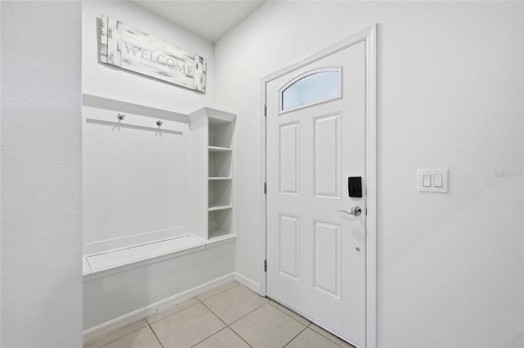 An entryway features a white door, tiled floor, and a built-in bench with shelving — 8929 SYDNEY AVENUE, KISSIMMEE, FL