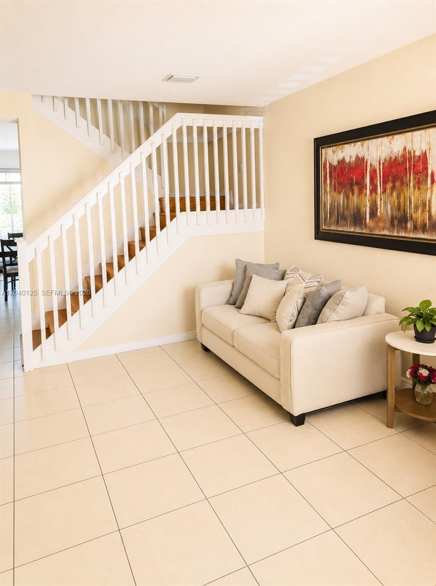 A beige sofa sits in a room with tiled floors and a white wooden staircase — 12488 SW 122nd St, Miami FL 33186, MIAMI, FL