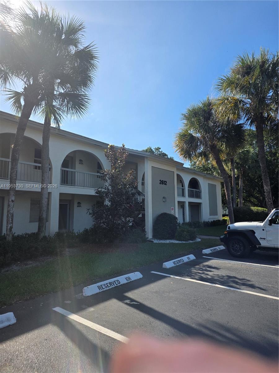 A two-story apartment building with arched balconies and palm trees in front of parking spaces — 2612 Nassau Bnd # E2, Coconut Creek FL 33066, COCONUT CREEK, FL