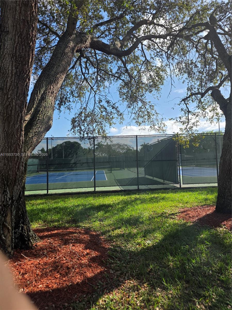 A view of a fenced tennis court framed by two large trees — 2612 Nassau Bnd # E2, Coconut Creek FL 33066, COCONUT CREEK, FL