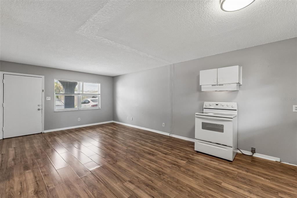 An unfurnished room with gray walls, wood-look flooring, a white stove, and a white door — 601 STATE AVENUE UNIT 2, HOLLY HILL, FL