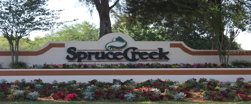 A sign for the Spruce Creek community stands in front of trees and flower beds — 17710 SE 105TH TERRACE, SUMMERFIELD, FL