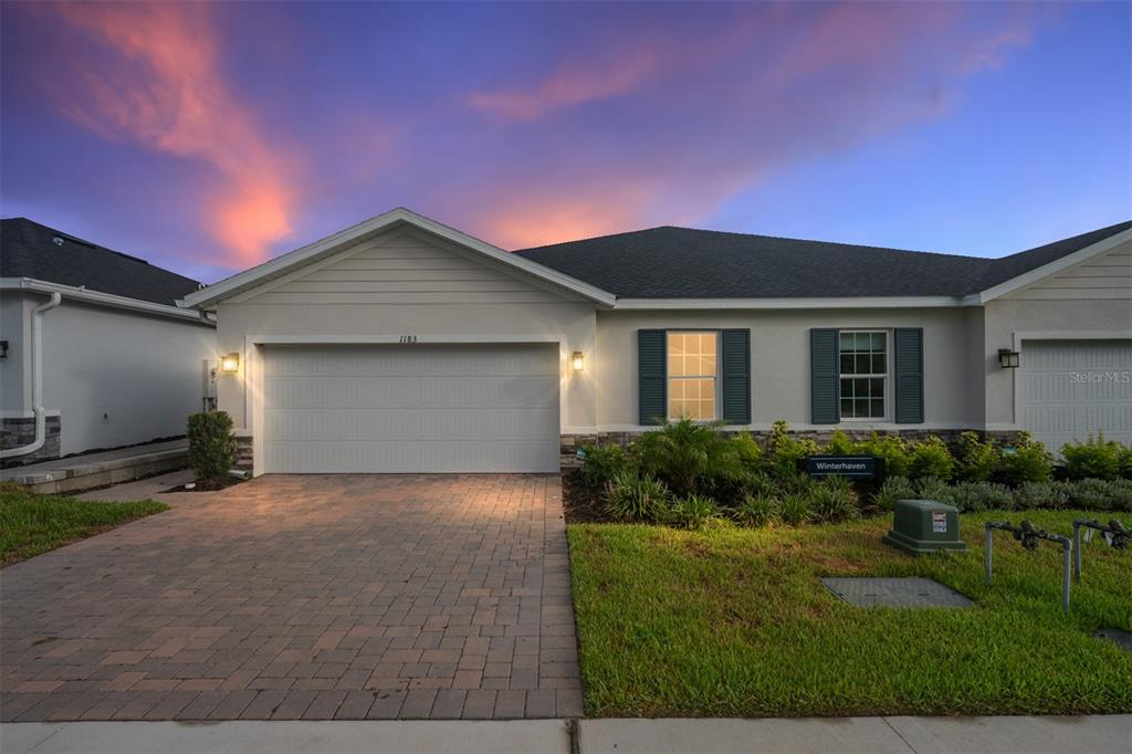 A single-story house with a paved driveway, two-car garage, and dark shutters at dusk — 1183 TURTLE ISLAND ROAD, LADY LAKE, FL
