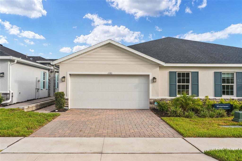 A single-story house with a two-car garage, beige stucco siding, and blue window shutters — 1183 TURTLE ISLAND ROAD, LADY LAKE, FL