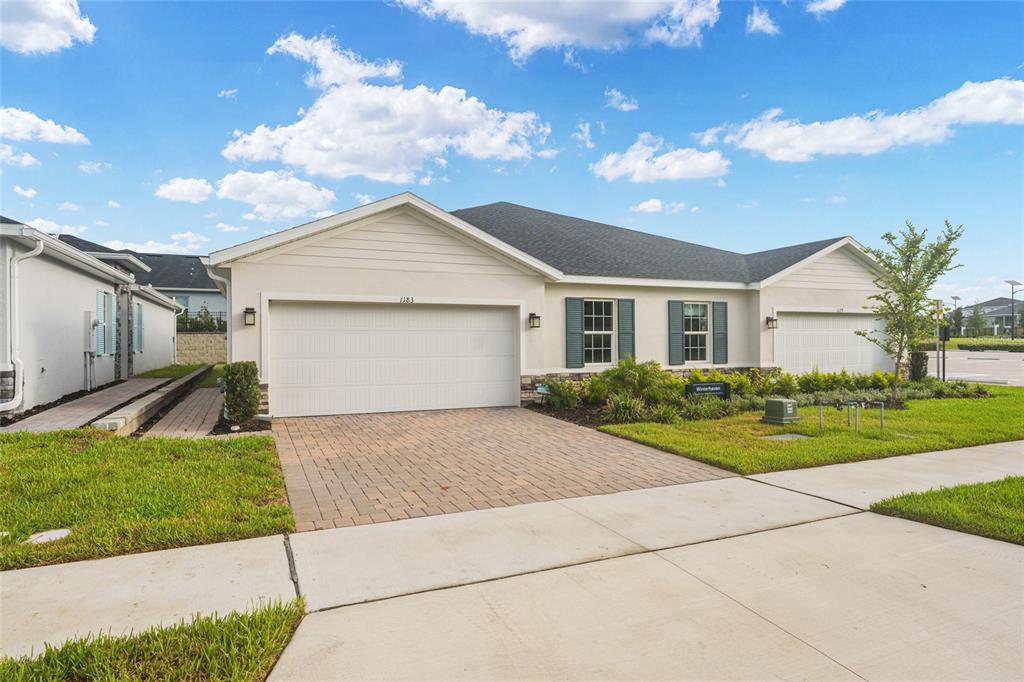 A single-story house with a two-car garage, beige siding, and a paved driveway — 1183 TURTLE ISLAND ROAD, LADY LAKE, FL