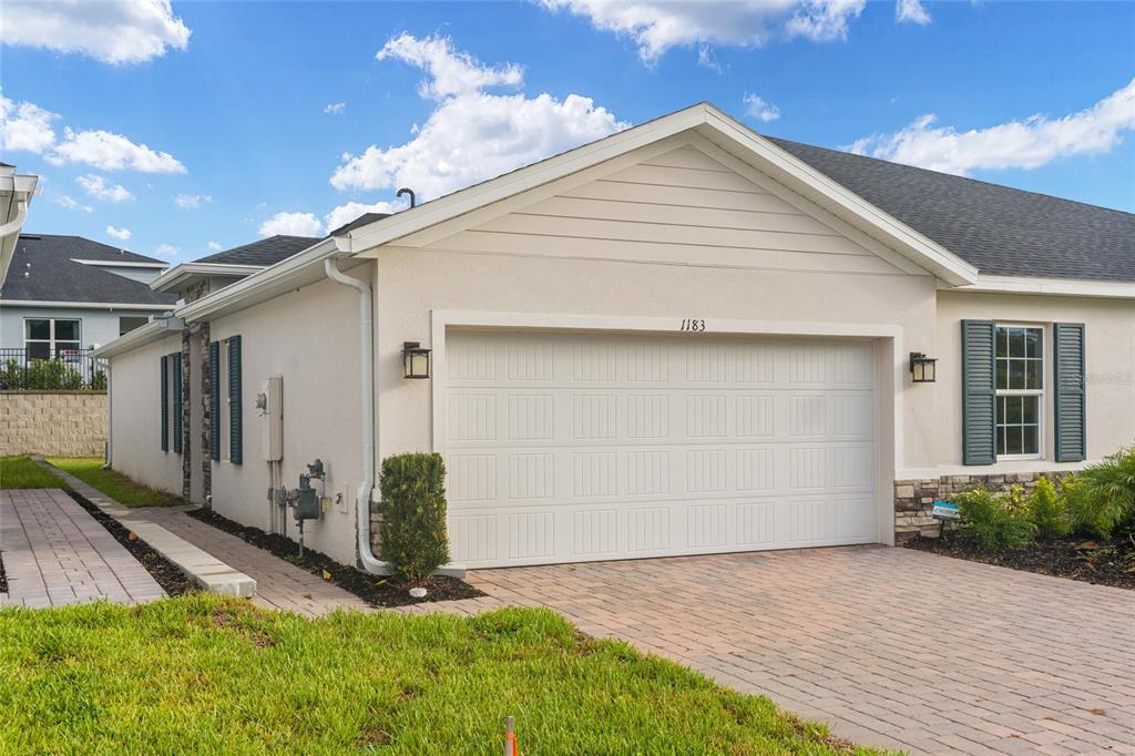 Exterior view of a house with a two-car garage, brick driveway, and beige stucco siding — 1183 TURTLE ISLAND ROAD, LADY LAKE, FL