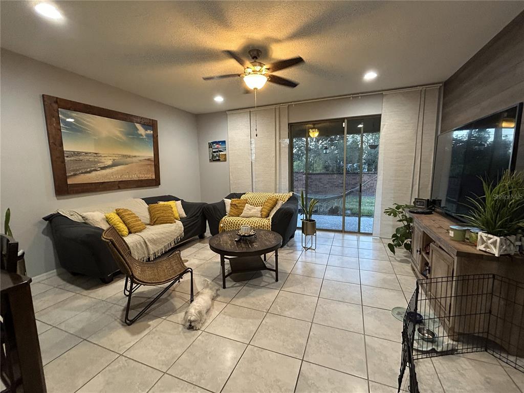A living room features tile flooring, two dark sofas with yellow pillows, and a sliding glass door — 10813 CORSICAN STREET UNIT 10, ORLANDO, FL