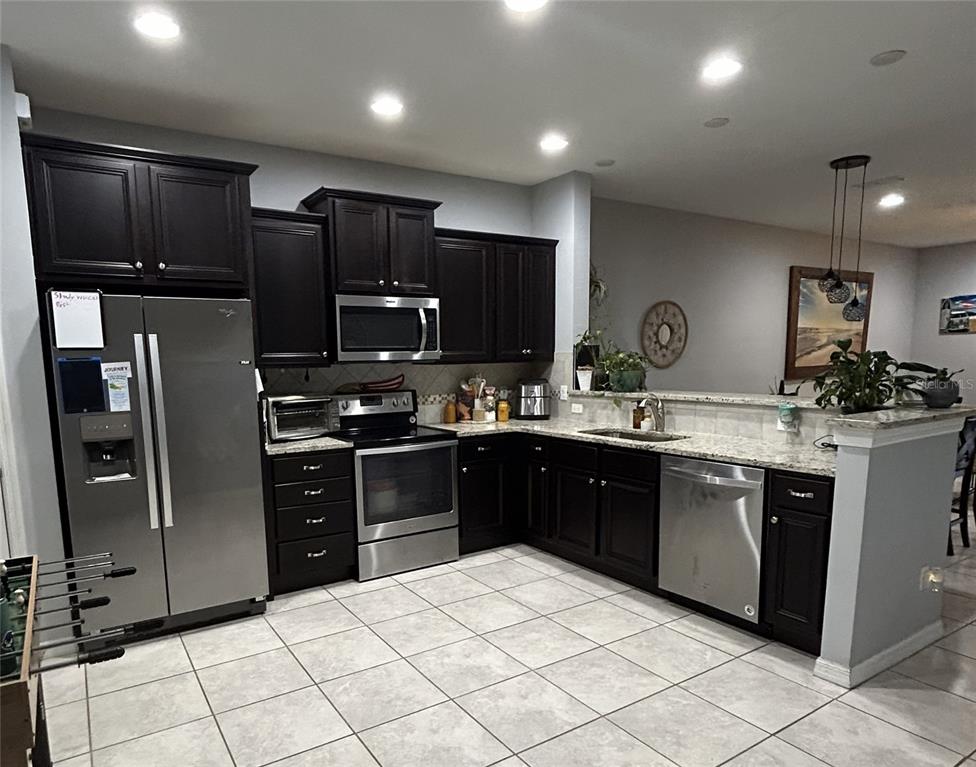 A kitchen features dark wood cabinets, stainless steel appliances, granite countertops, and light tile flooring — 10813 CORSICAN STREET UNIT 10, ORLANDO, FL
