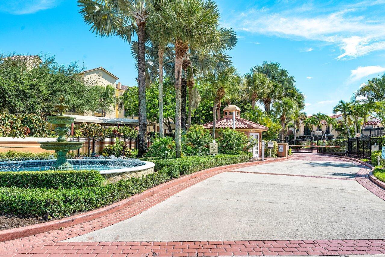 A gated entrance features a tiered fountain, palm trees, and a guardhouse under a blue sky — 300 Uno Lago Drive # 304, Juno Beach FL 33408, JUNO BEACH, FL