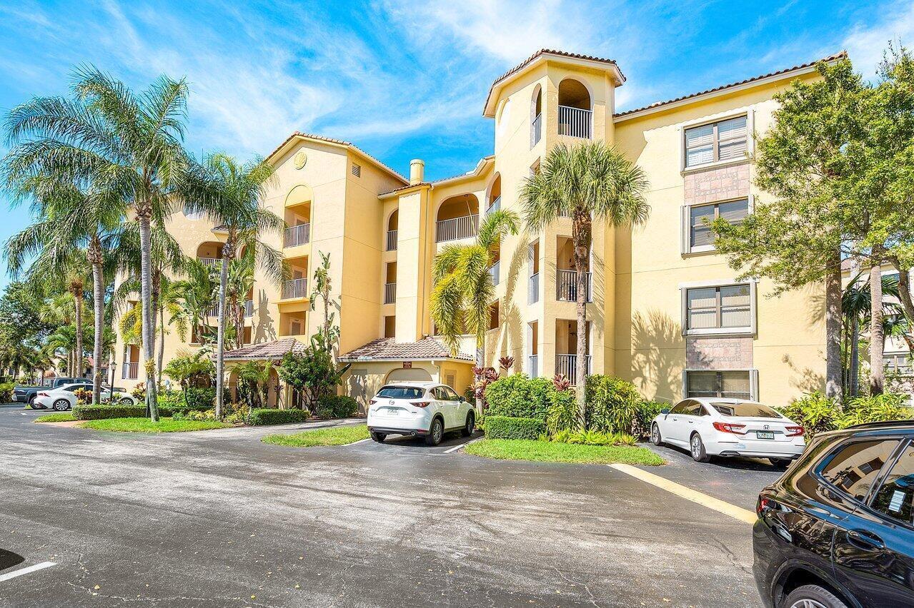 A multi-story yellow apartment building with palm trees and parked cars in the foreground — 300 Uno Lago Drive # 304, Juno Beach FL 33408, JUNO BEACH, FL