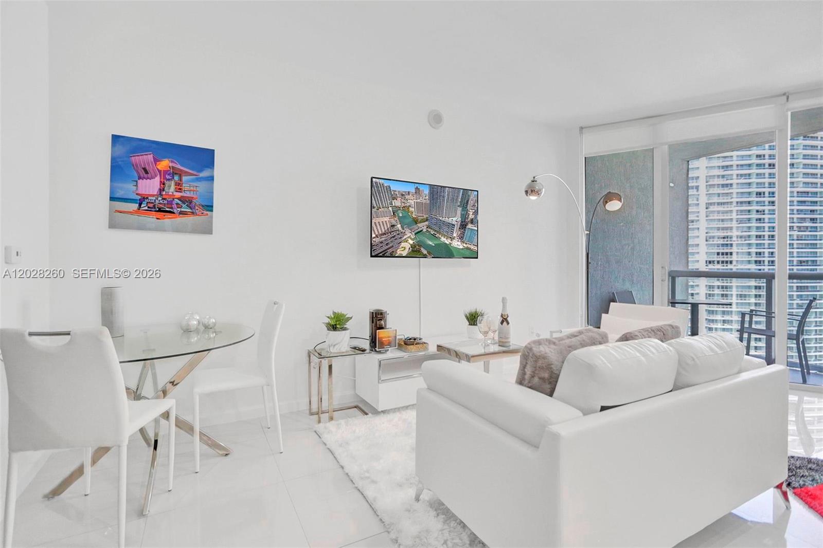 A bright living room features white furniture, a glass dining table, and a wall-mounted television — 475 Brickell Ave # 3408, Miami FL 33131, MIAMI, FL