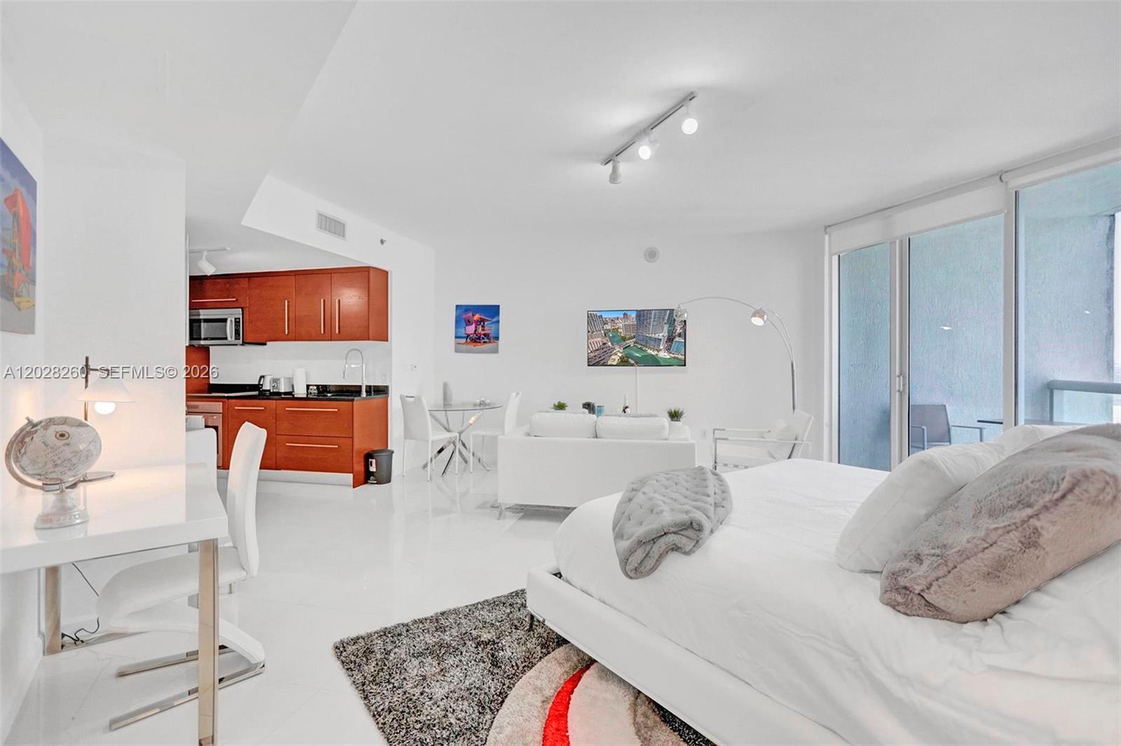 This studio apartment features a white interior, a kitchen with wood cabinets, and a bed — 475 Brickell Ave # 3408, Miami FL 33131, MIAMI, FL