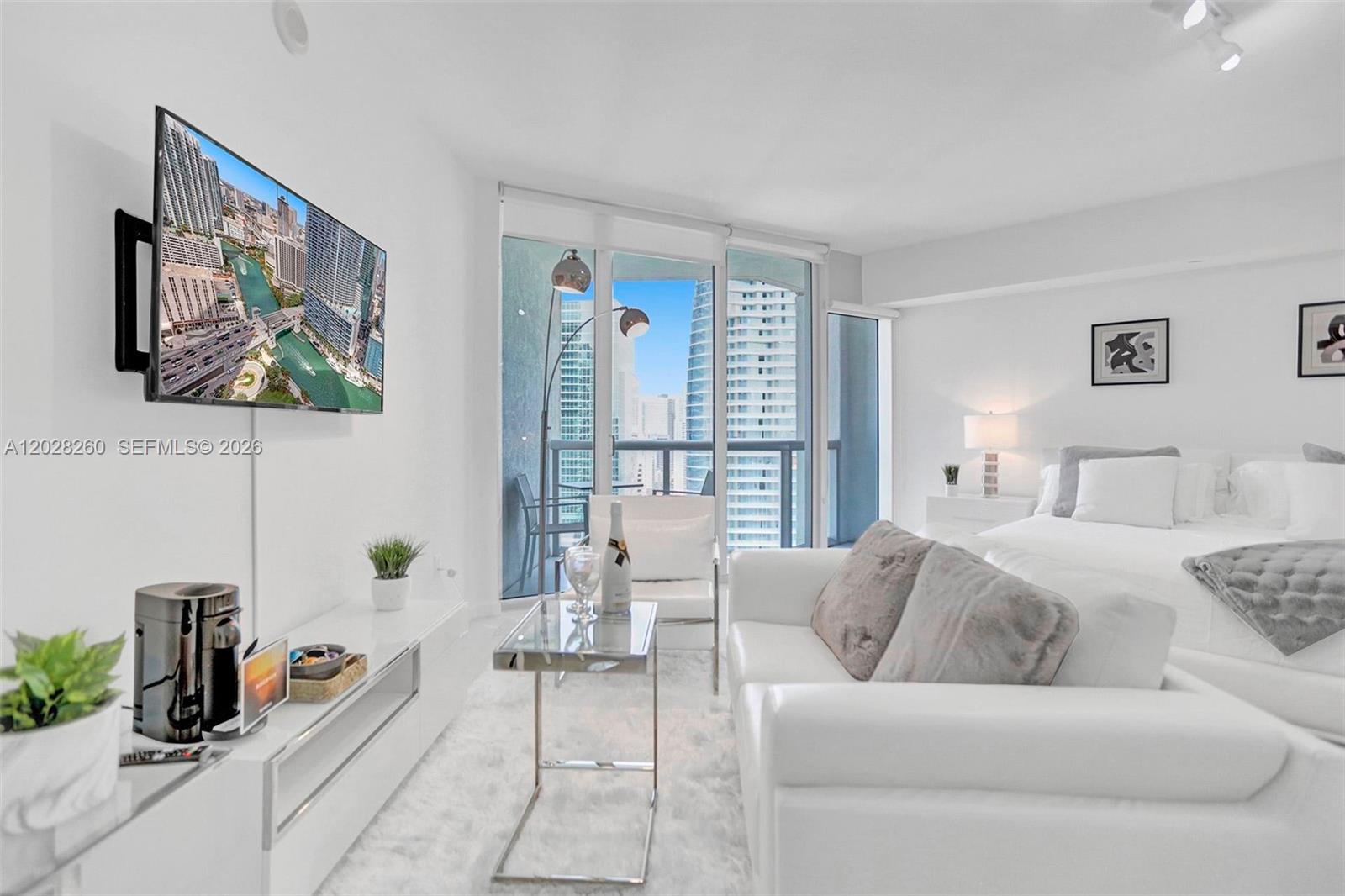 A modern studio apartment features a white sofa, a bed, and a balcony with city views — 475 Brickell Ave # 3408, Miami FL 33131, MIAMI, FL