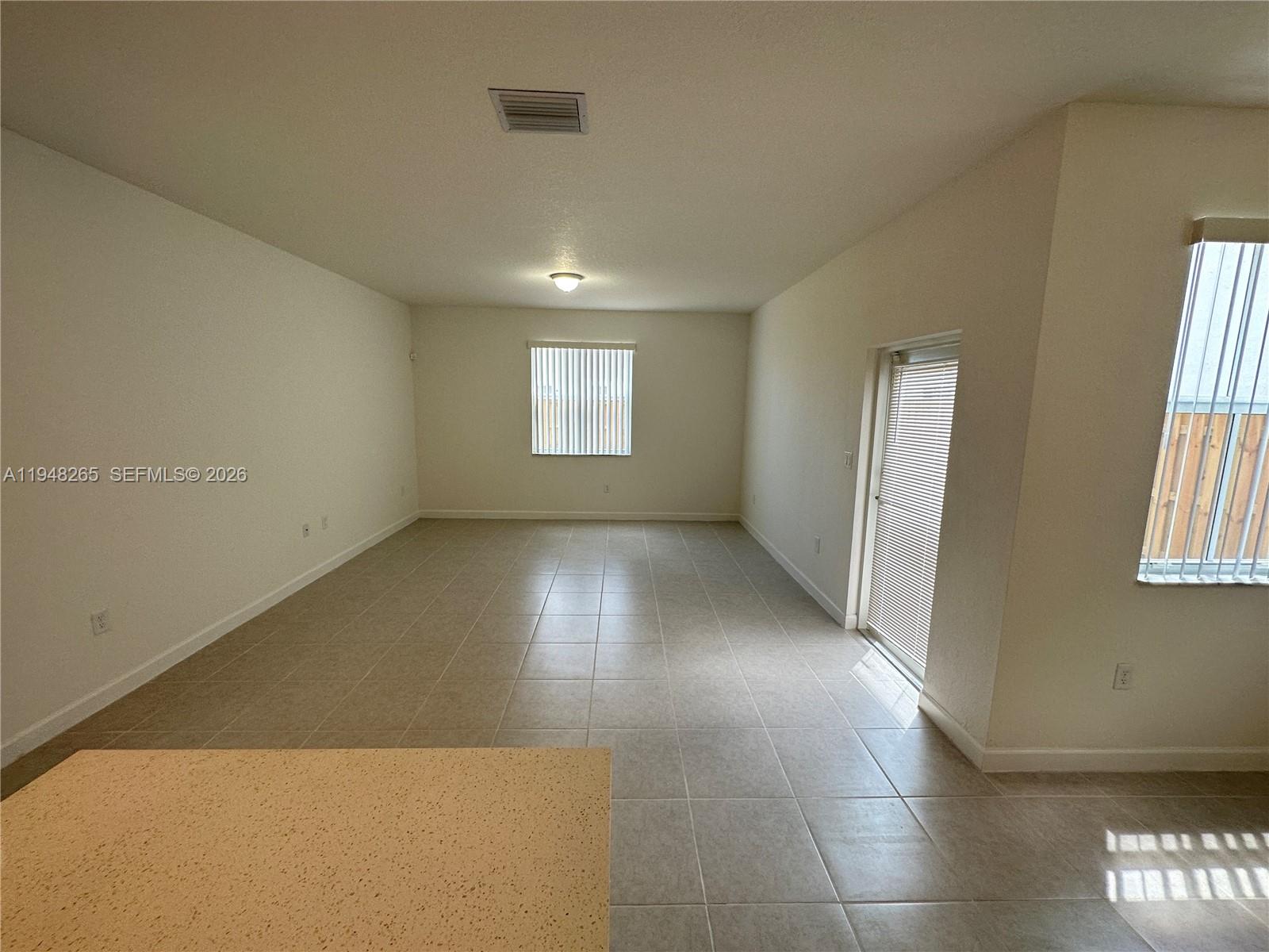 An empty room features light-colored tile flooring, white walls, a sliding glass door, and windows — 2382 NW 131st Cir, Miami FL 33167, MIAMI, FL