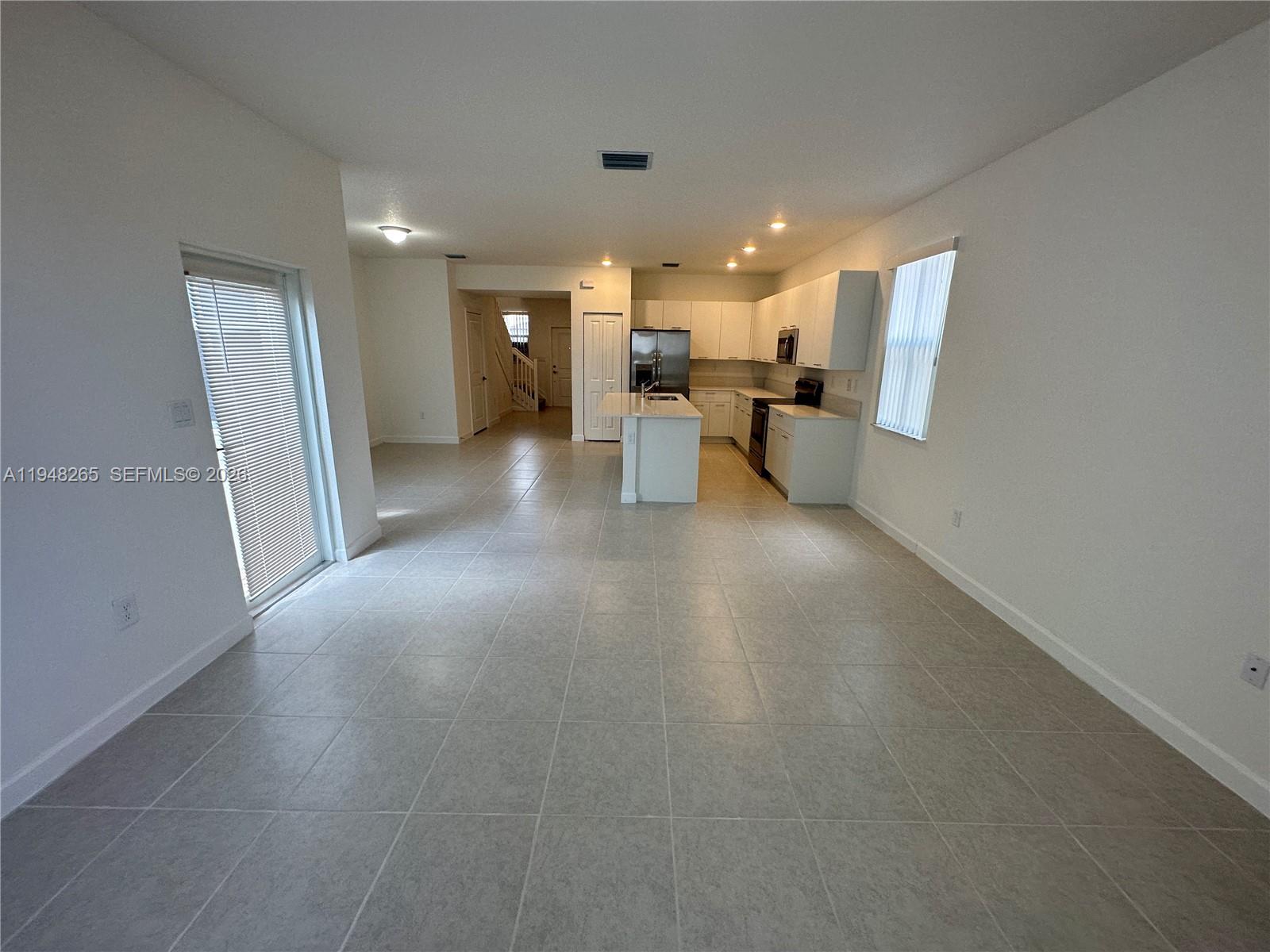 An open-concept kitchen with white cabinets and a central island features light-colored tile flooring — 2382 NW 131st Cir, Miami FL 33167, MIAMI, FL