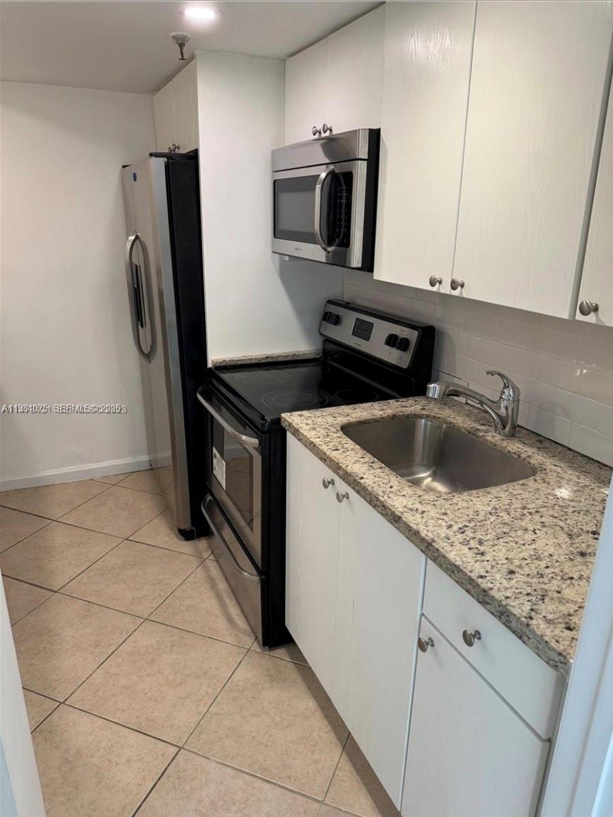 A galley kitchen features stainless steel appliances, white cabinets, and speckled granite countertops — 20850 San Simeon Way # 5, Miami FL 33179, MIAMI, FL