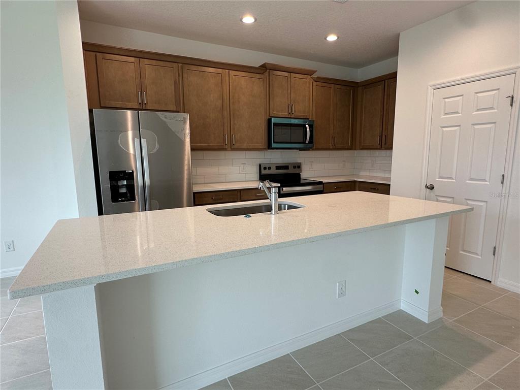 A kitchen features a large island with a sink, stainless steel appliances, and wood cabinets — 676 BIRDSWILL LANE, DELAND, FL