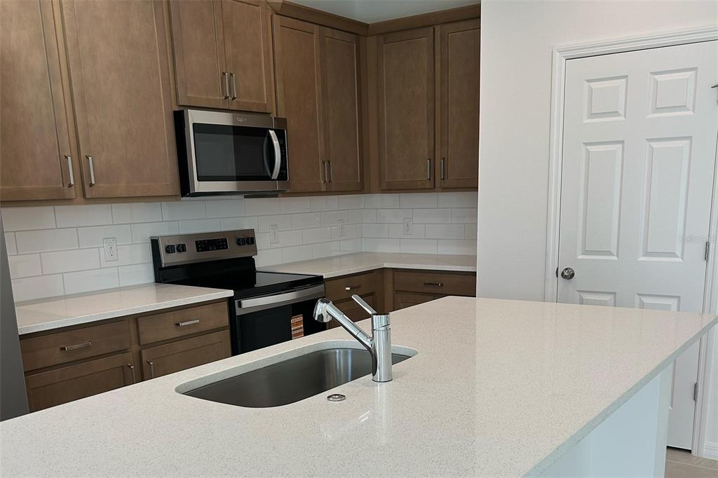 A kitchen features wood cabinets, white countertops, a subway tile backsplash, and a center island — 676 BIRDSWILL LANE, DELAND, FL