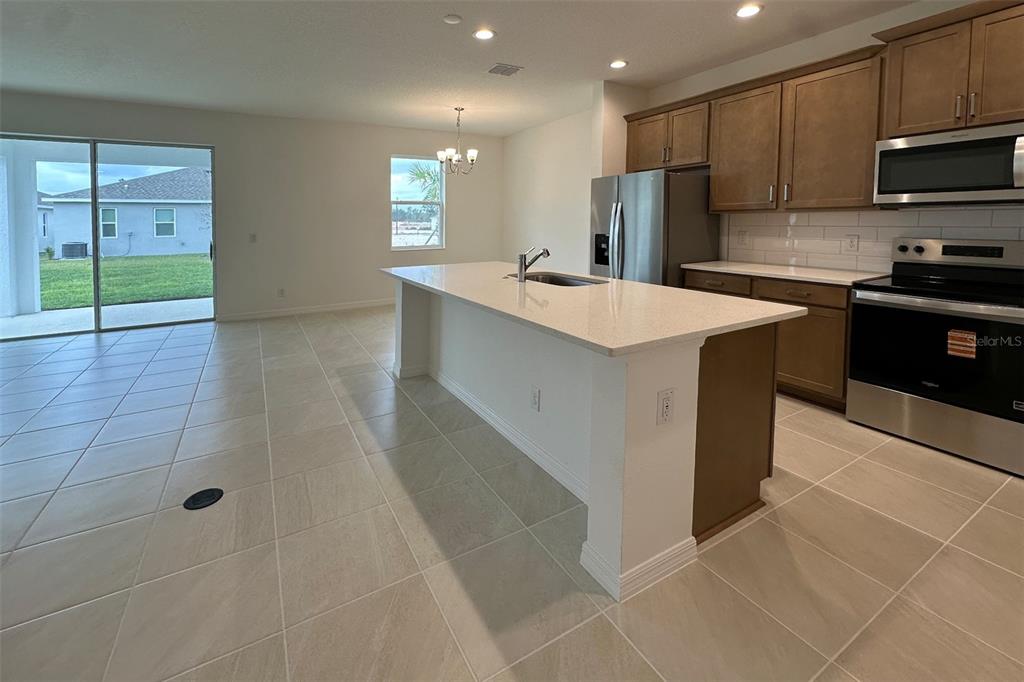 A kitchen with a central island, light-colored countertops, brown cabinets, and tile flooring — 676 BIRDSWILL LANE, DELAND, FL