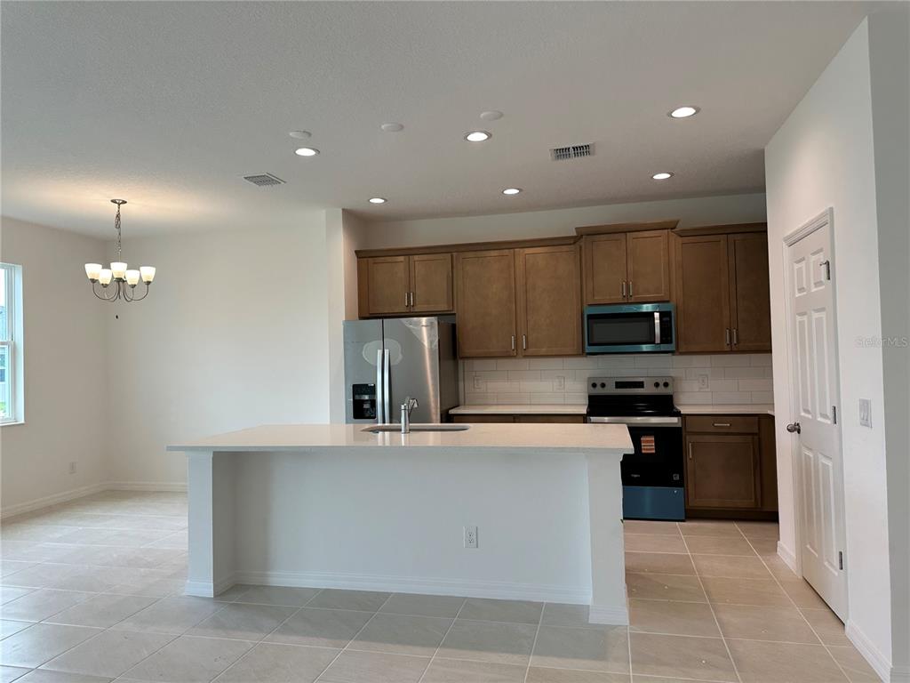 A kitchen features brown cabinets, stainless steel appliances, a white island, and tile flooring — 676 BIRDSWILL LANE, DELAND, FL