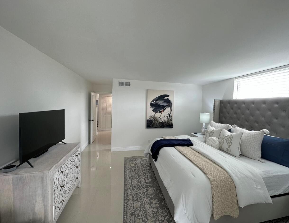 A bedroom features a tufted gray headboard, a white dresser, and a large bird painting — 14773 Cumberland Drive # 3010, Delray Beach FL 33446, DELRAY BEACH, FL