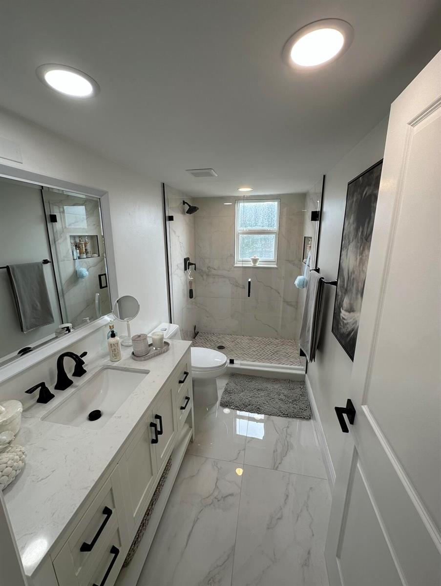 A modern bathroom features a white vanity, marble-look tile flooring, and a glass-enclosed walk-in shower — 14773 Cumberland Drive # 3010, Delray Beach FL 33446, DELRAY BEACH, FL