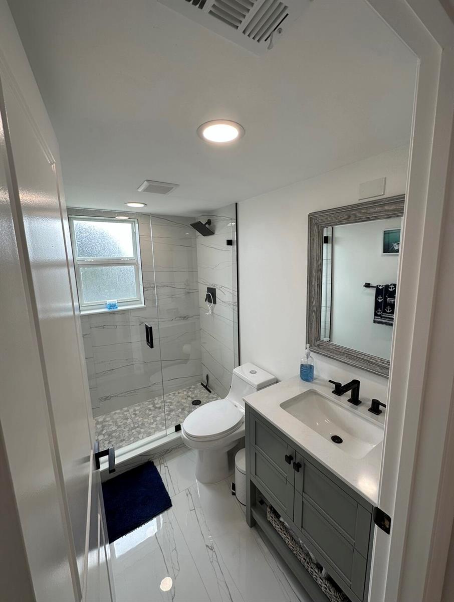 A modern bathroom features a glass-enclosed walk-in shower, a gray vanity, and white marble-look flooring — 14773 Cumberland Drive # 3010, Delray Beach FL 33446, DELRAY BEACH, FL