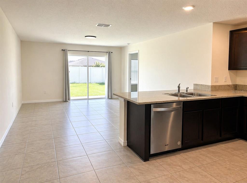A kitchen with dark cabinets and granite countertops overlooks a tiled living area with sliding doors — 16511 MOSAIC OAR DRIVE, WIMAUMA, FL