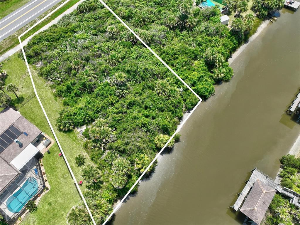 An aerial view shows a vacant, vegetated waterfront lot outlined in white next to houses — 3502 N OCEAN SHORE BOULEVARD, PALM COAST, FL
