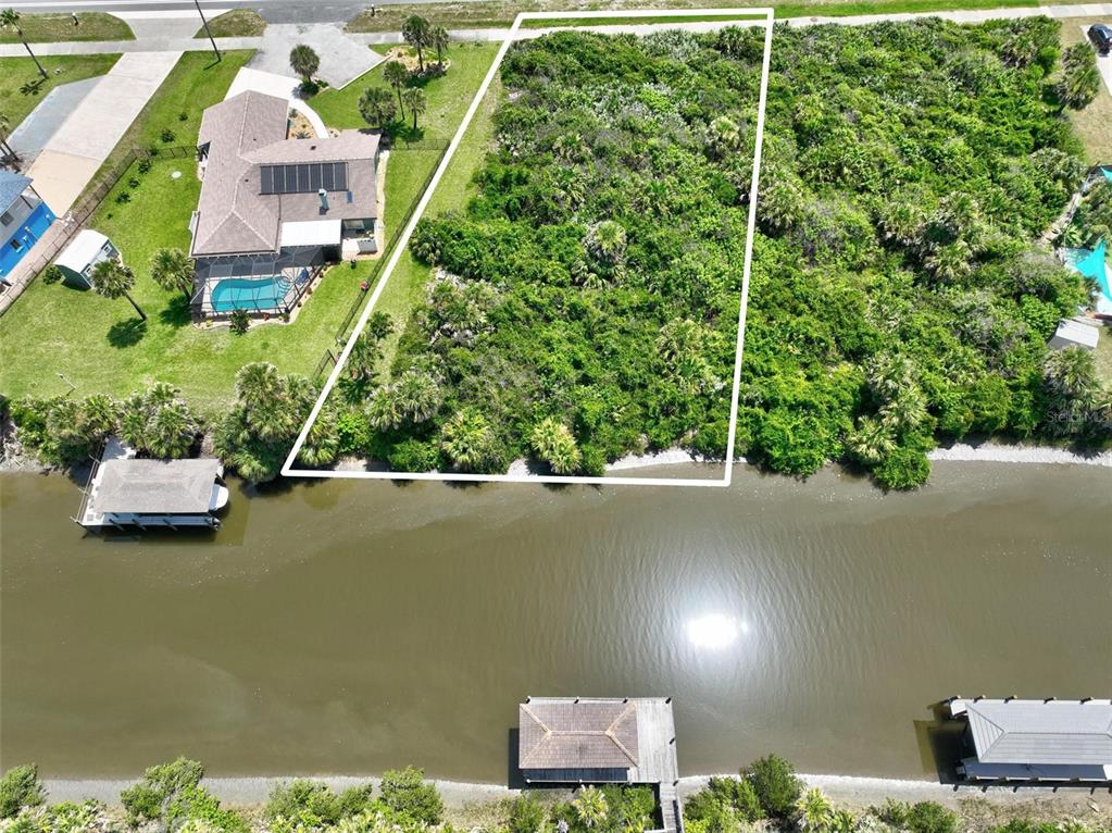 An aerial view shows a vacant, wooded waterfront lot outlined in white next to a house — 3502 N OCEAN SHORE BOULEVARD, PALM COAST, FL