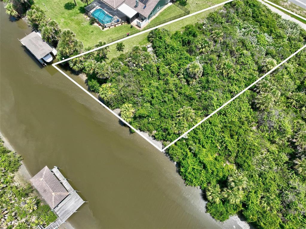 An aerial view shows a vacant, wooded waterfront lot outlined in white next to a canal — 3502 N OCEAN SHORE BOULEVARD, PALM COAST, FL