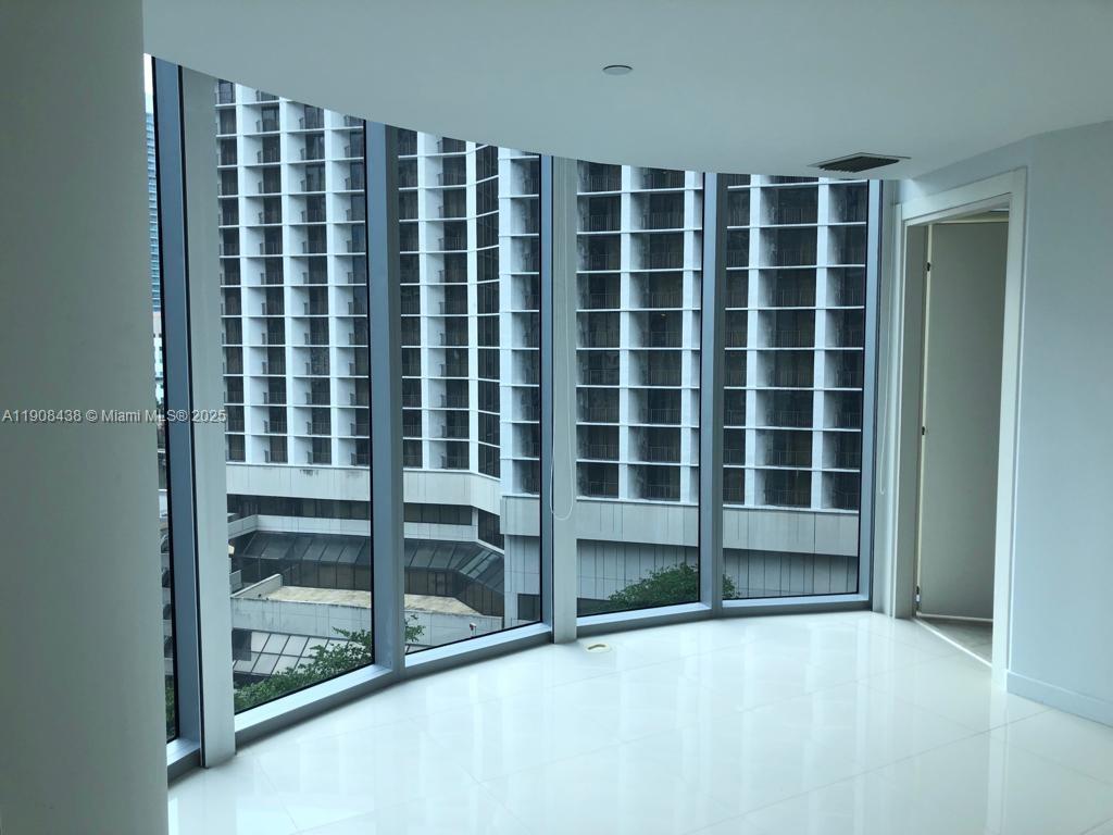 An empty room with white tile floors and floor-to-ceiling windows overlooking a neighboring building — 200 Biscayne Boulevard Way # 902, Miami FL 33131, MIAMI, FL