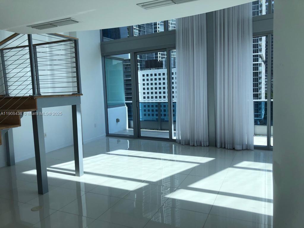 A bright, modern living room features white tile floors, a lofted staircase, and floor-to-ceiling windows — 200 Biscayne Boulevard Way # 902, Miami FL 33131, MIAMI, FL
