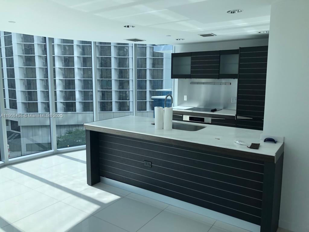 A modern kitchen features a dark wood island, white countertops, and floor-to-ceiling windows — 200 Biscayne Boulevard Way # 902, Miami FL 33131, MIAMI, FL