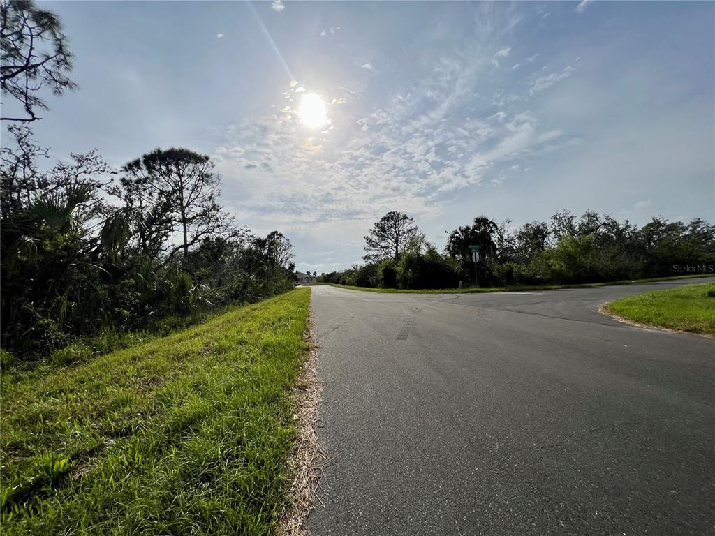 A paved road curves through a grassy, wooded area under a bright, sunny sky — 15163 ESTATE TERRACE, PORT CHARLOTTE, FL