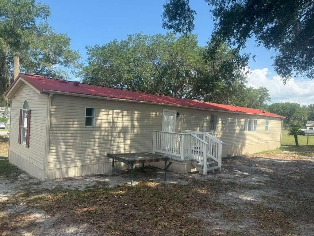 A beige mobile home with a red metal roof and a small white wooden deck — 1650 BELMONT AVENUE UNIT 29, MULBERRY, FL
