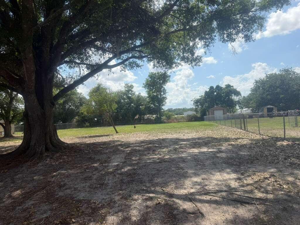 A large tree shades a sandy foreground leading to a grassy, fenced-in backyard — 1650 BELMONT AVENUE UNIT 29, MULBERRY, FL