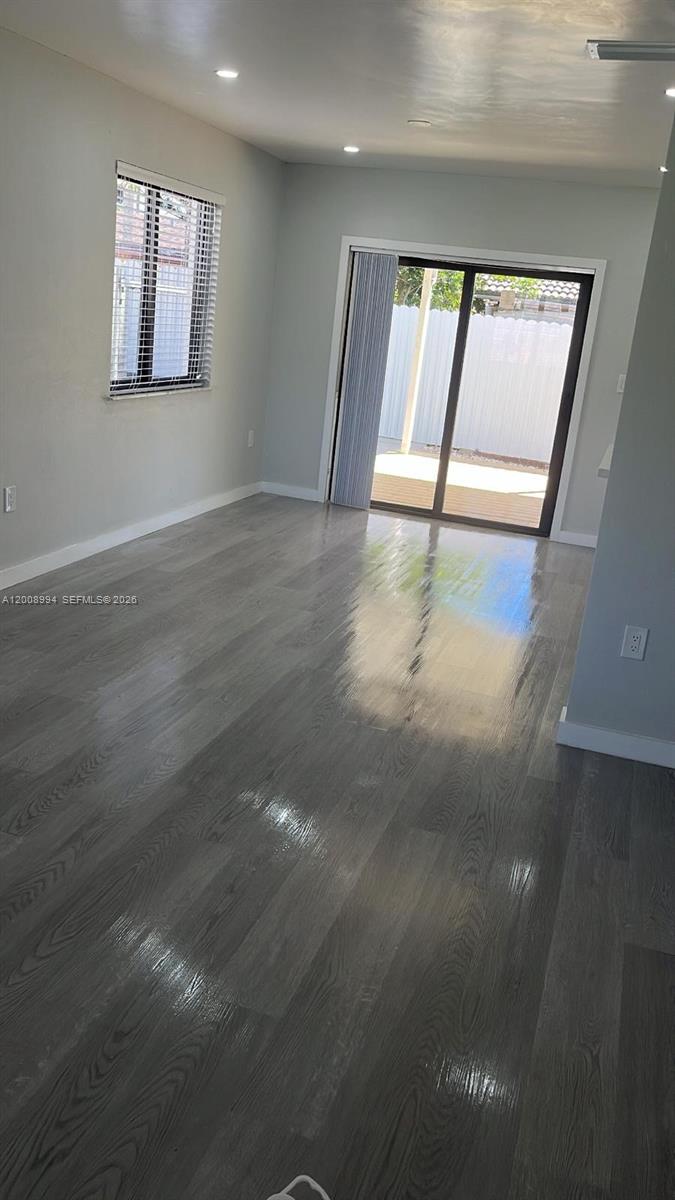 An empty room features gray wood-look flooring, light gray walls, a window, and sliding doors — SWEETWATER, FL