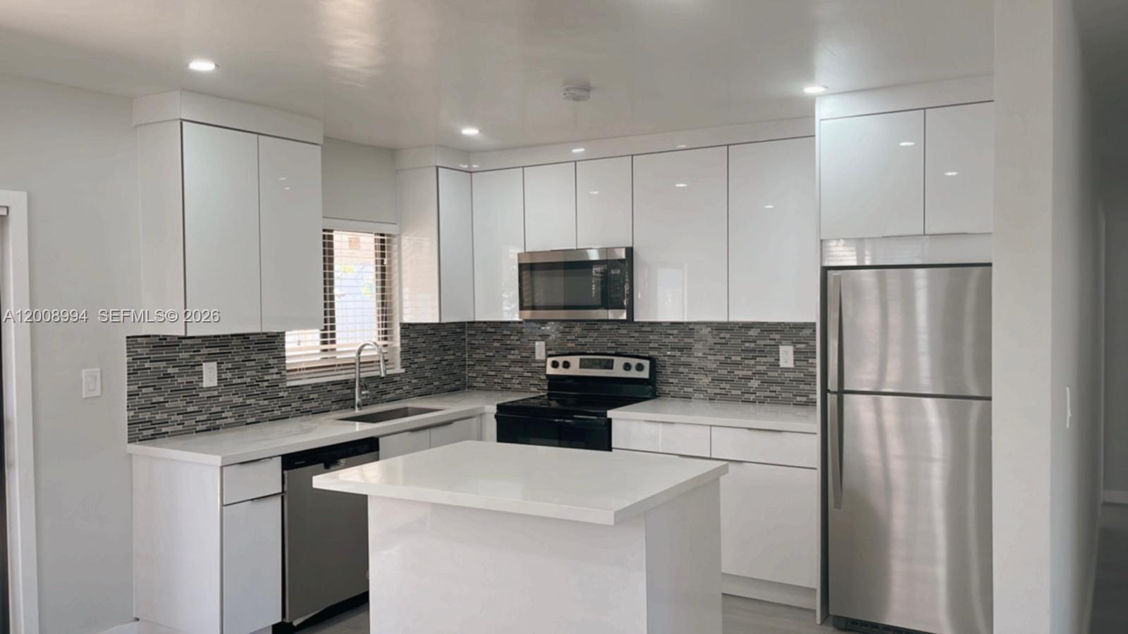 A modern kitchen features white cabinets, stainless steel appliances, a kitchen island, and tiled backsplash — SWEETWATER, FL