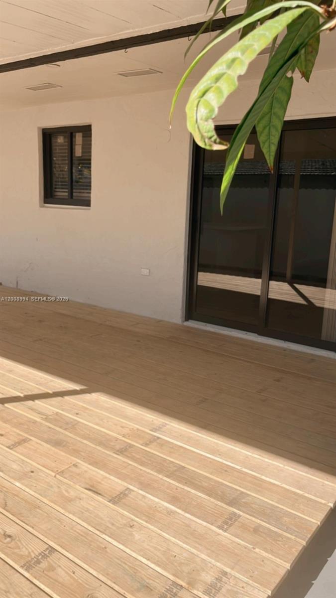 A wooden deck extends from a white exterior wall with a window and sliding door — SWEETWATER, FL
