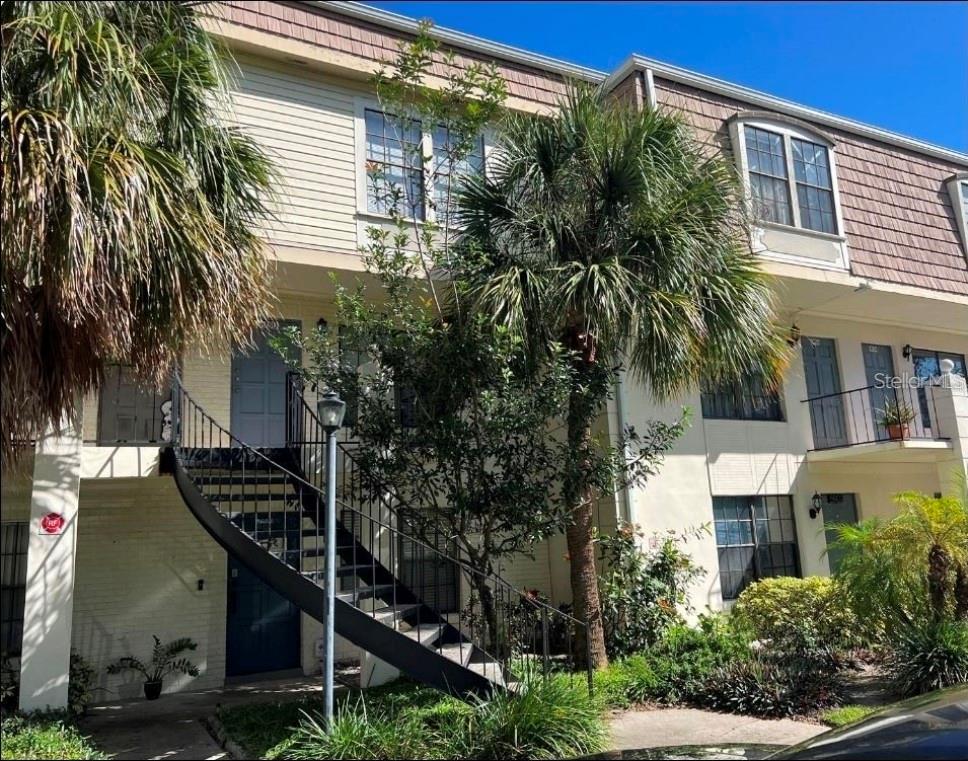 Exterior view of a two-story apartment building with a metal staircase and palm trees — 5930 VILLAGE CIRCLE UNIT GE, ORLANDO, FL
