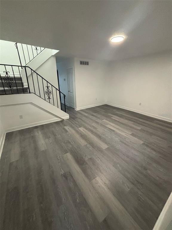 An empty room with gray wood-look flooring, white walls, and a staircase with black railings — 5930 VILLAGE CIRCLE UNIT GE, ORLANDO, FL